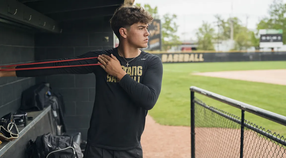 Teen pitcher stretching resistance bands outdoors at a baseball field, early morning light