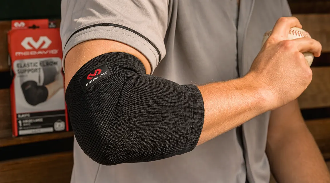 Close-up of a teen pitcher's elbow with a black compression sleeve fitted snugly, hand gripping a baseball mid-warm-up toss