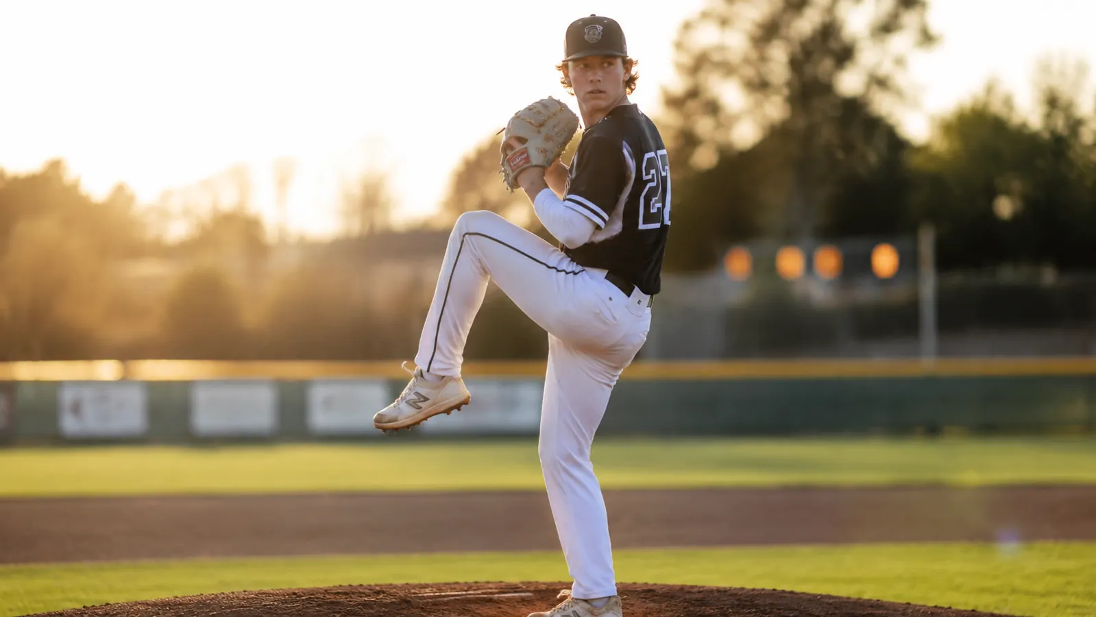 Teen pitcher winding up on the mound, strong and healthy, sun behind him