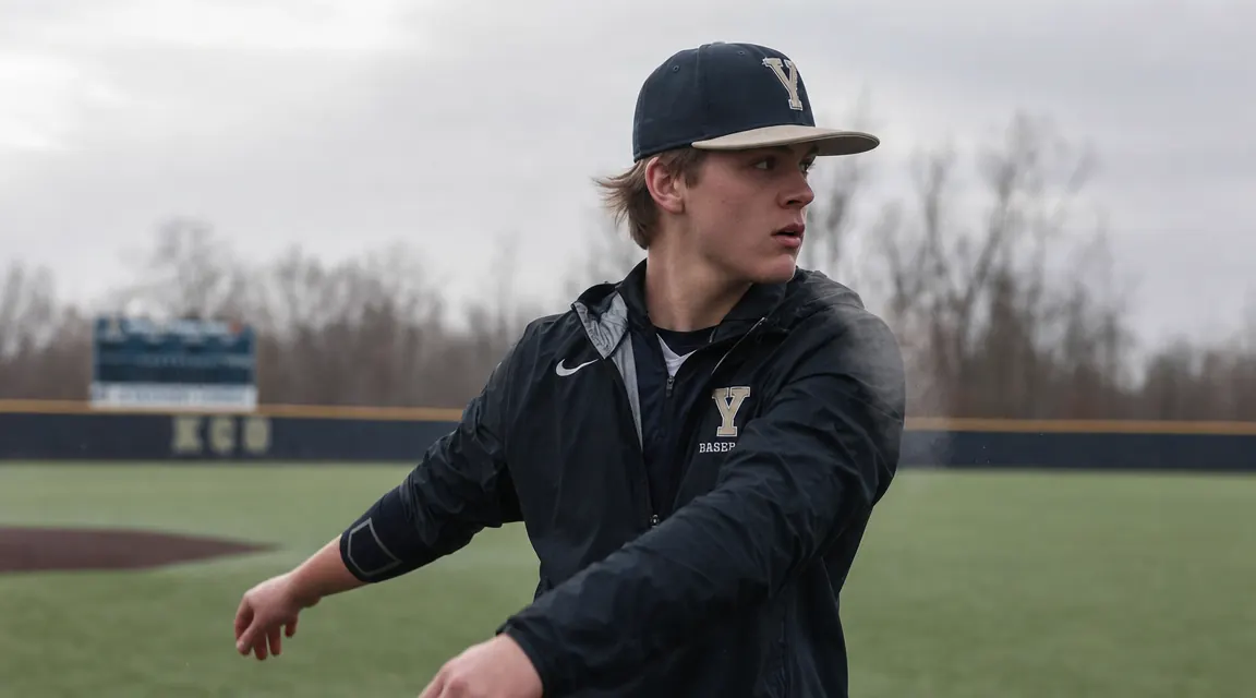 Teen pitcher warming up in cold weather, elbow sleeve visible under jersey during a spring morning practice